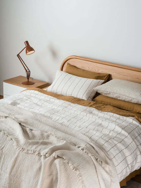 Monday Linen Duvet- Chalk/Miso Stripe on a bed with brown accent pillows and a modern bedside lamp.